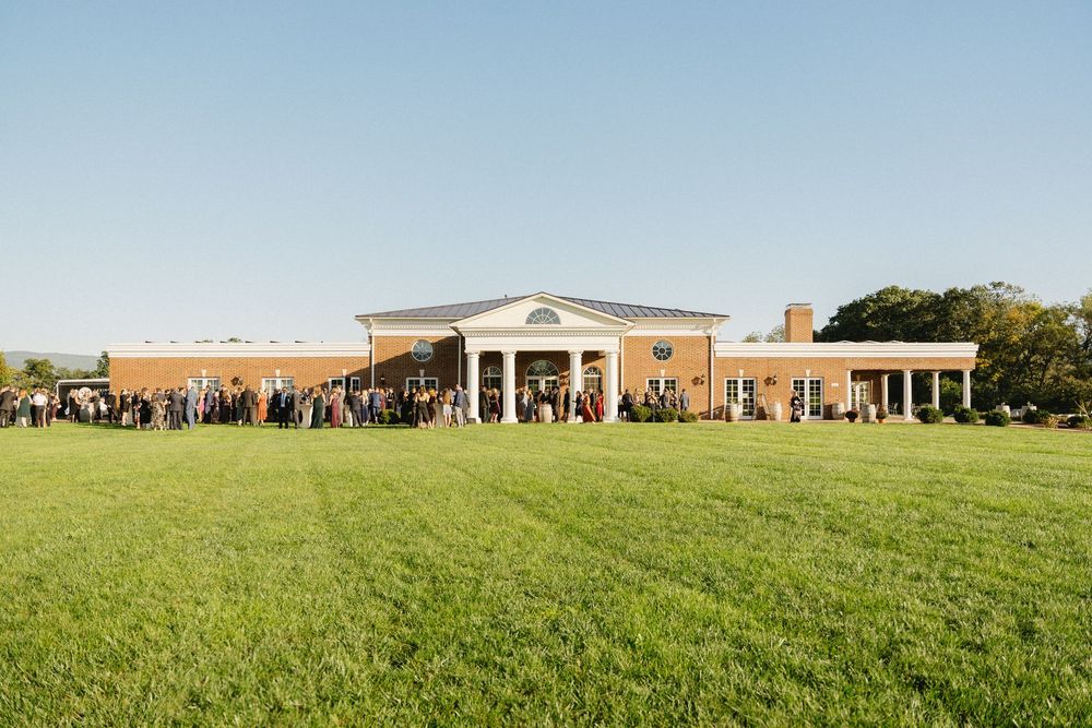 A classic brick wedding venue with white columns and a sprawling green lawn in summer.