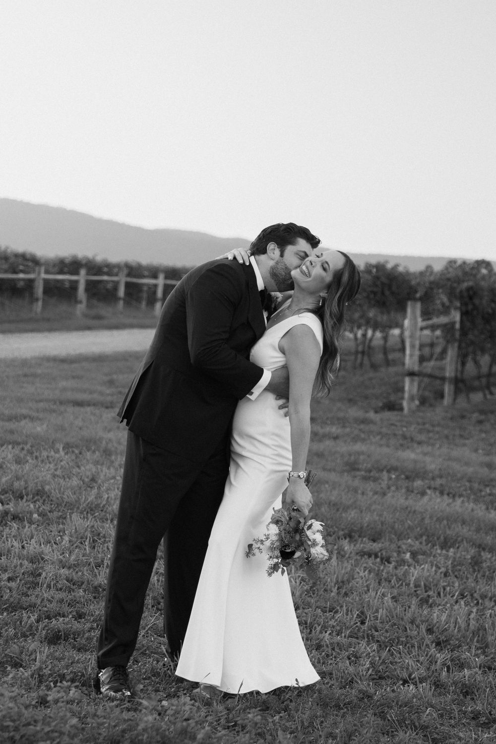 Romantic black and white portrait of couple embracing in vineyard landscape.