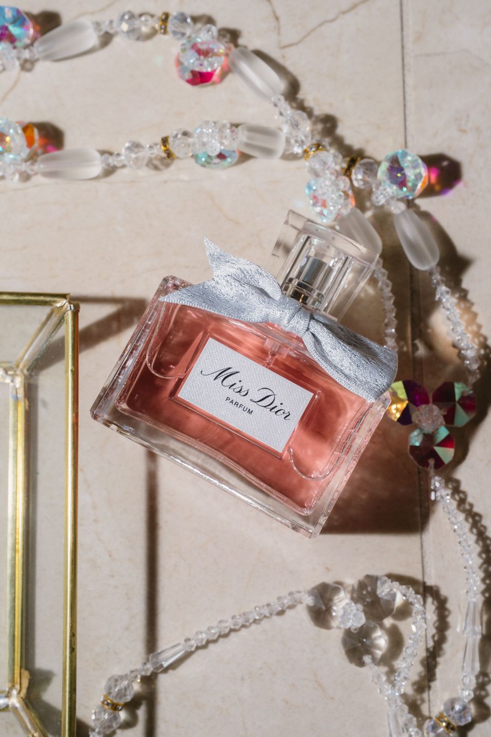 Elegant perfume bottles and jewelry arranged on a light beige surface with crystal accents.