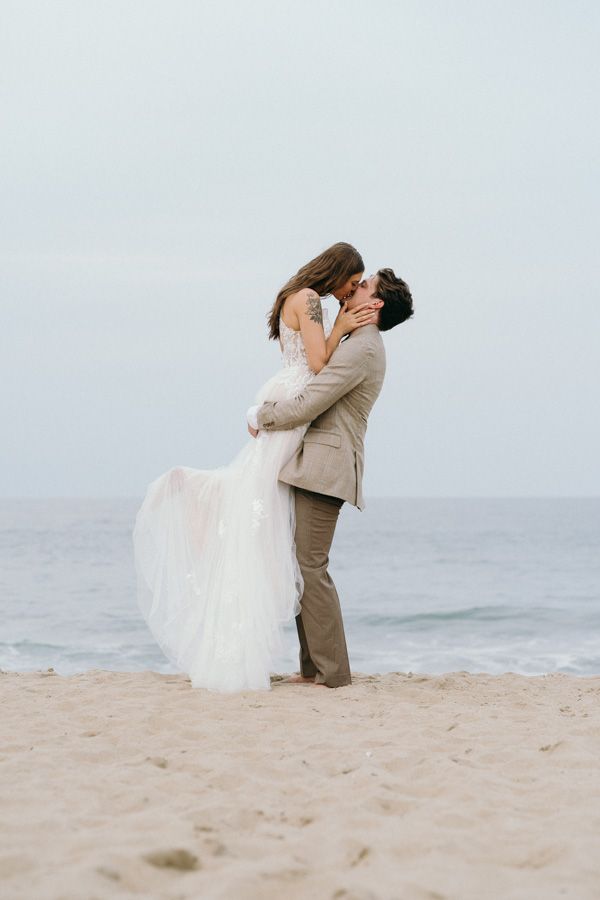 A romantic beach wedding photo series showing a couple embracing in their wedding attire on a misty shoreline.