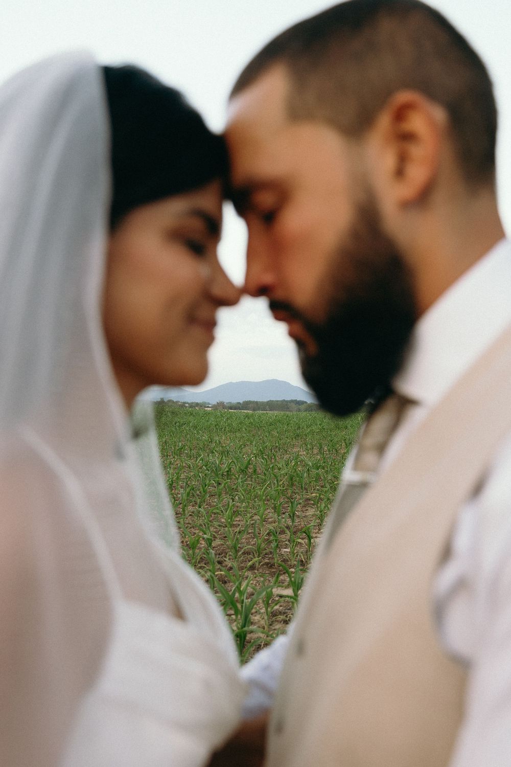 Romantic close-up of newlyweds sharing an intimate moment in a field with soft veil details.