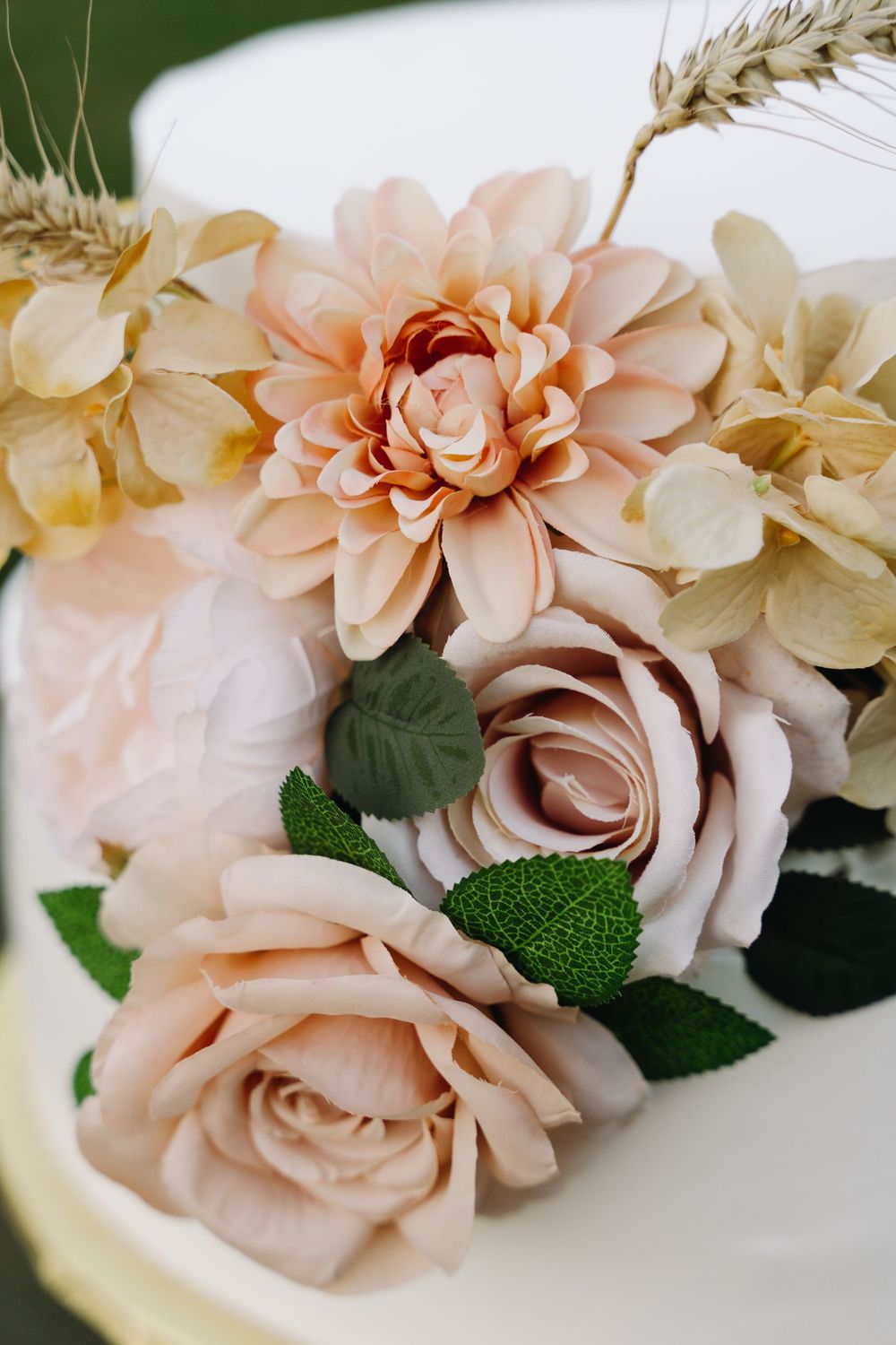 Elegant floral arrangement with peach roses and dahlias with wheat accents on white surface.