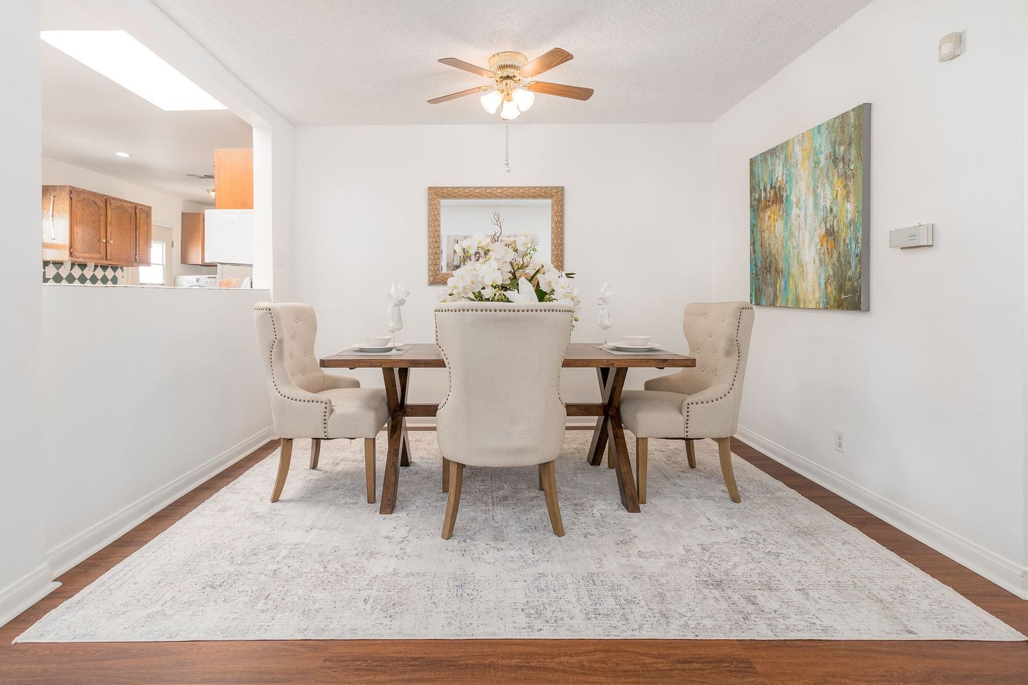 Modern open concept living room with white walls, light carpeting, and dining area featuring a ceiling fan.
