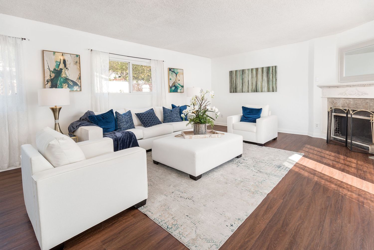 Modern living room with white couches, blue accent pillows, and hardwood floors in an open concept space.