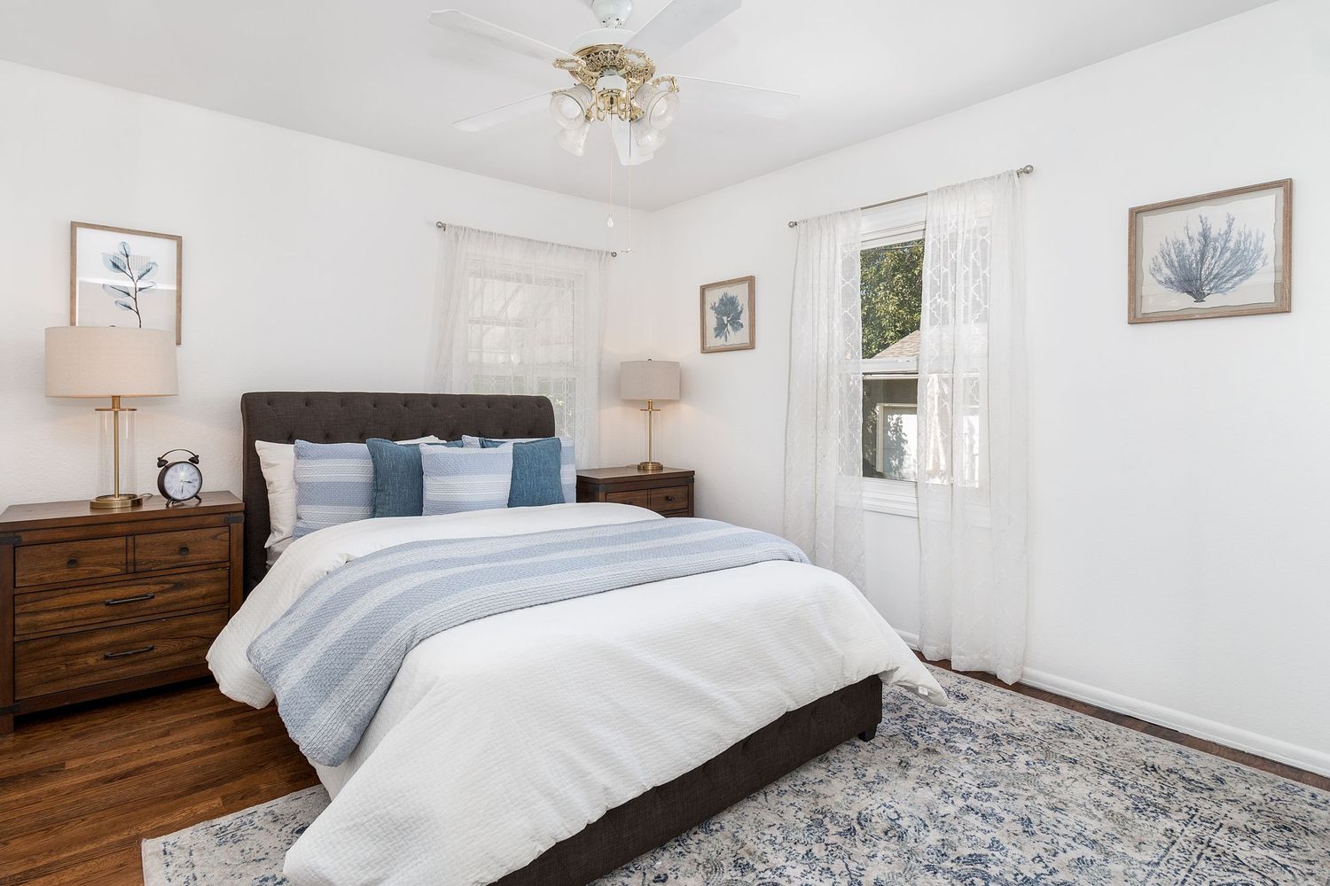 Bright bedroom with white bedding, dark wood furniture, and natural light streaming through windows.
