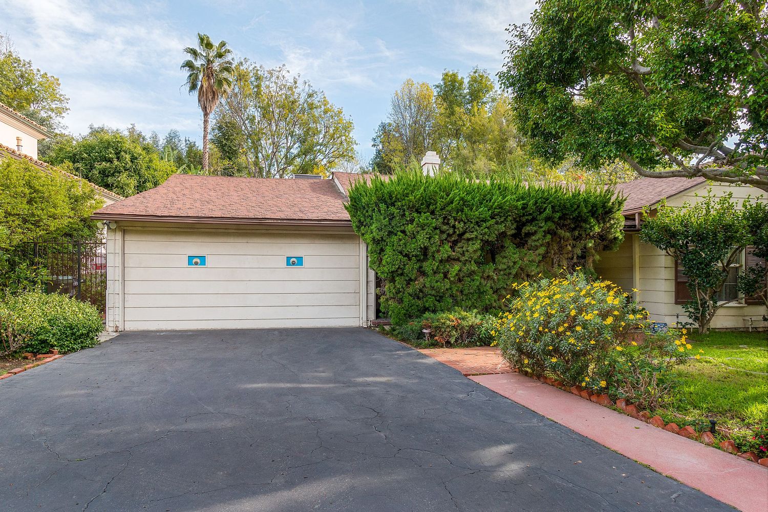 Long driveway leading to garage with landscaped yard and palm trees.