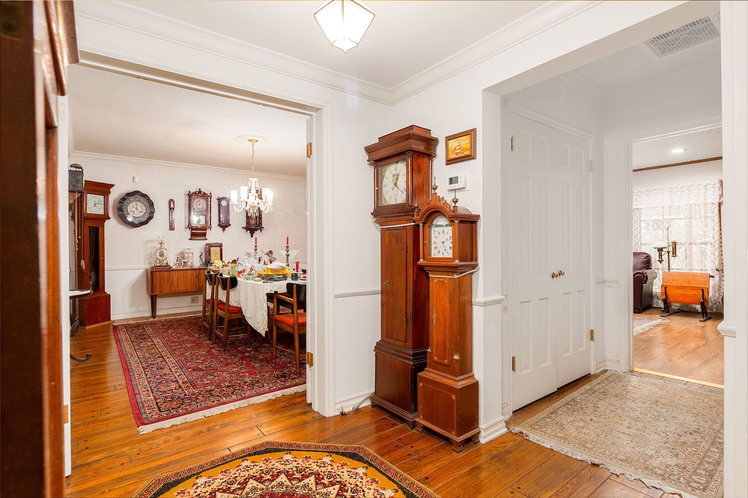 Long hallway with white walls showcasing vintage clocks and wooden furniture pieces.