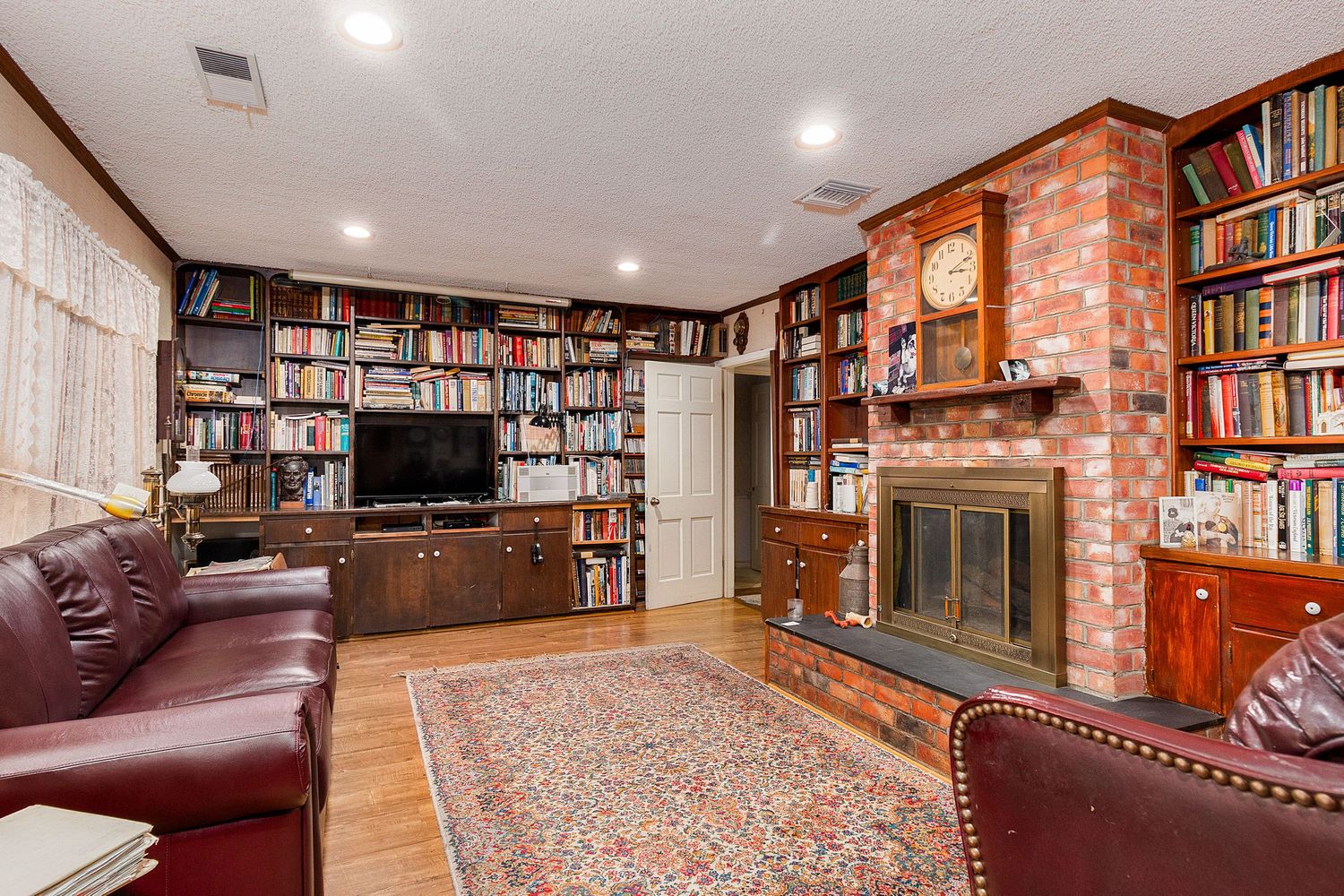 Cozy library room with exposed brick walls, built-in wooden bookshelves, and leather seating.