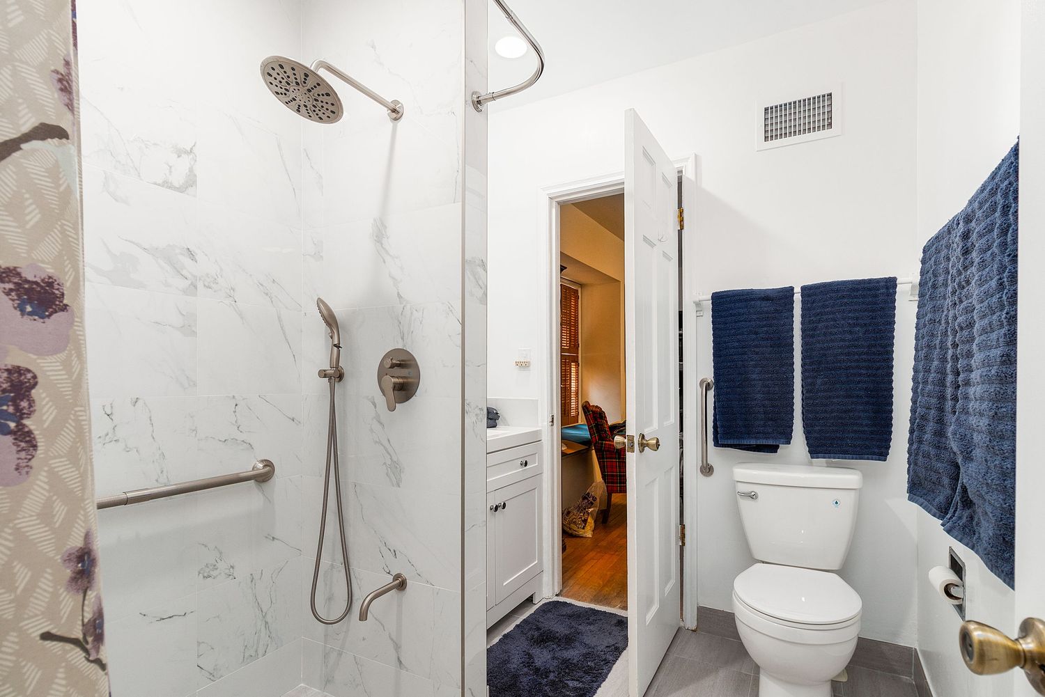 Modern white bathroom with glass shower enclosure and marble-look walls.