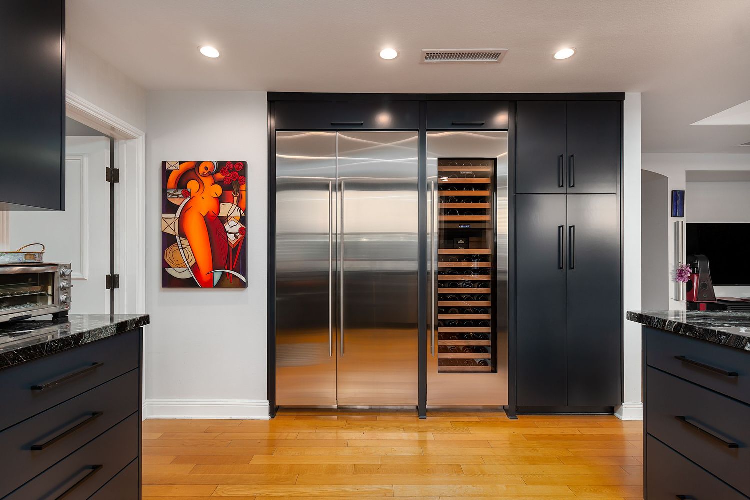 Contemporary kitchen with black cabinets, stainless steel appliances, and vibrant wall art.