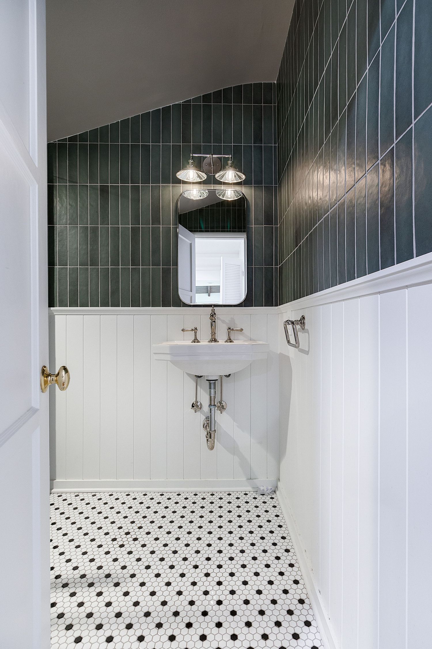 Stylish bathroom with dark green tile walls, white wainscoting, and polka dot floor pattern.