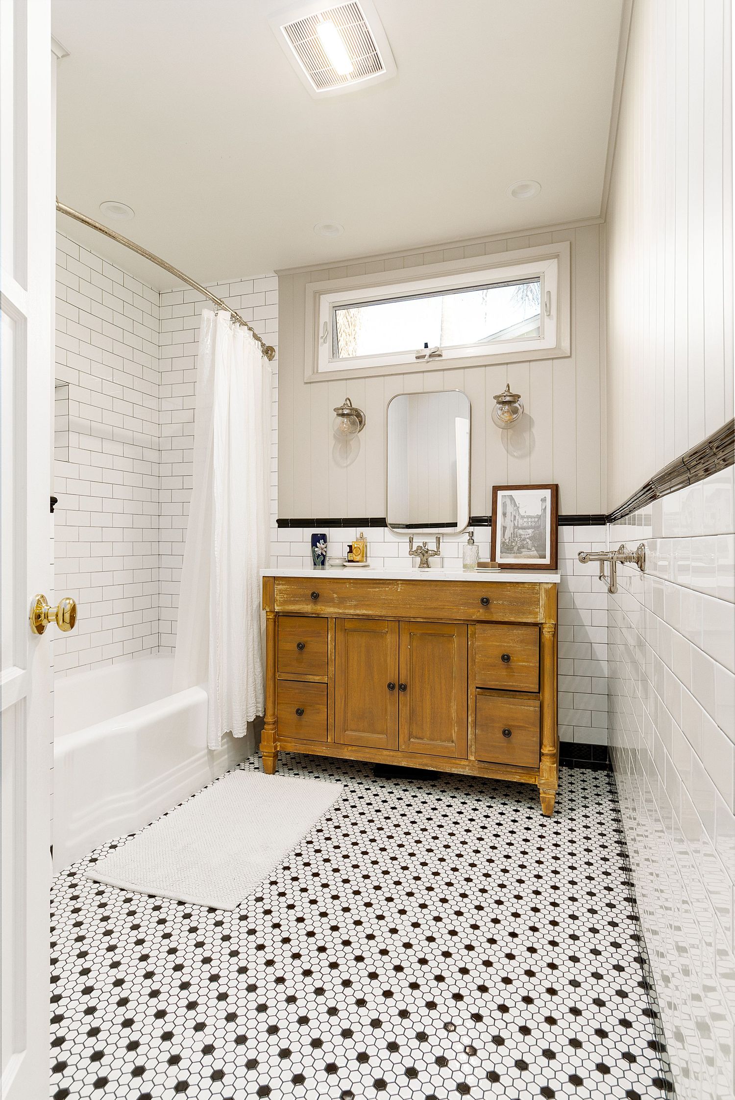 Spacious bathroom with wooden vanity, black and white tile flooring, and subway tile walls.