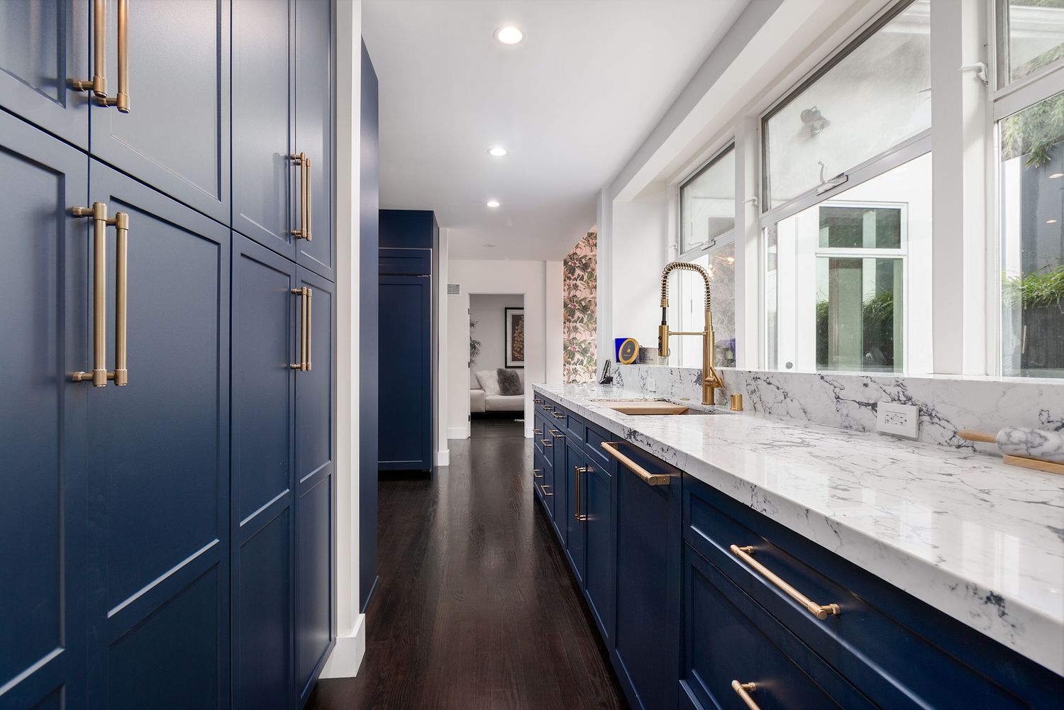 Long hallway with navy blue cabinets and white walls features modern recessed lighting.