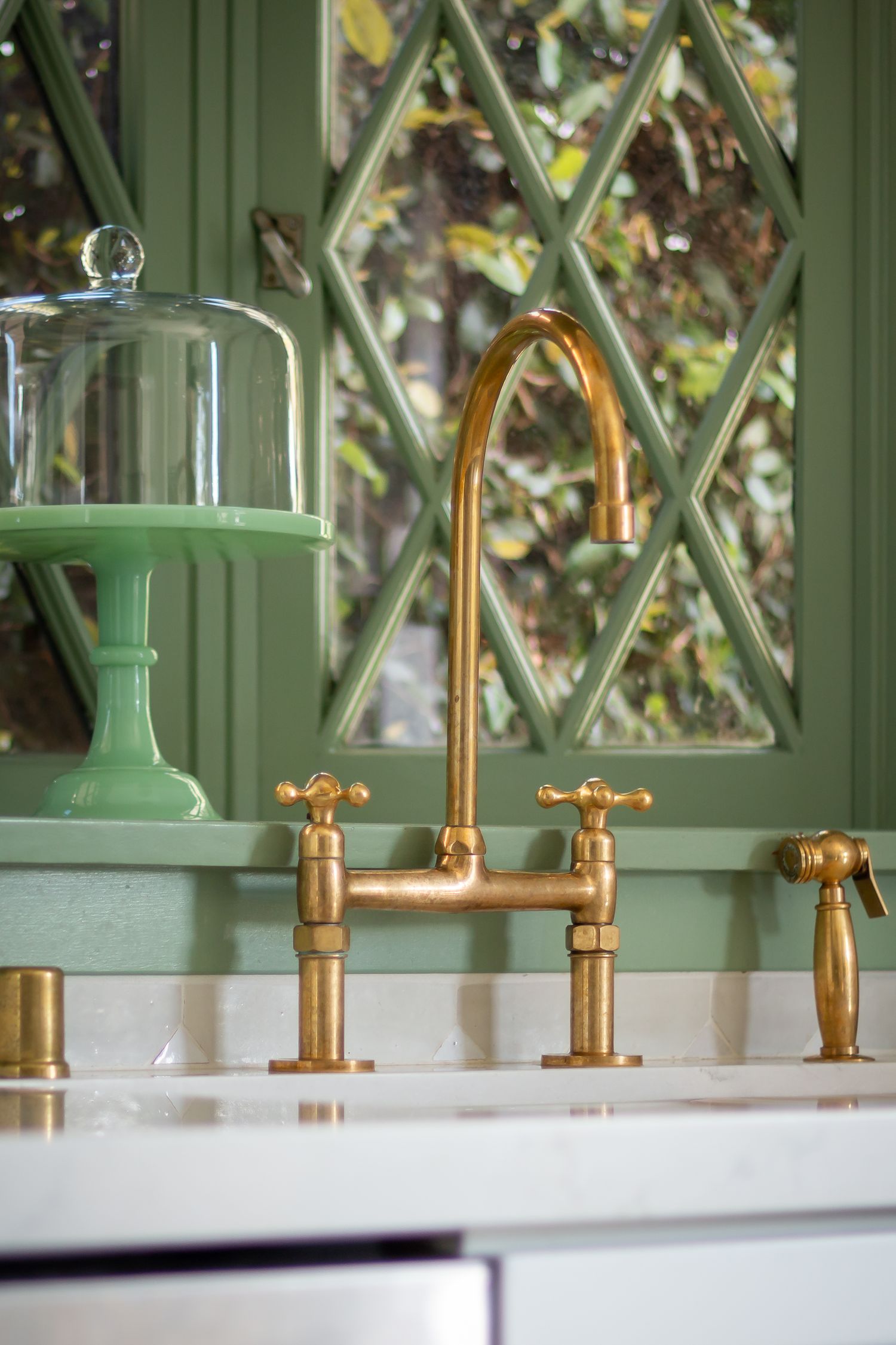 Brass bridge faucet with cross handles against diamond pane window and white countertop.