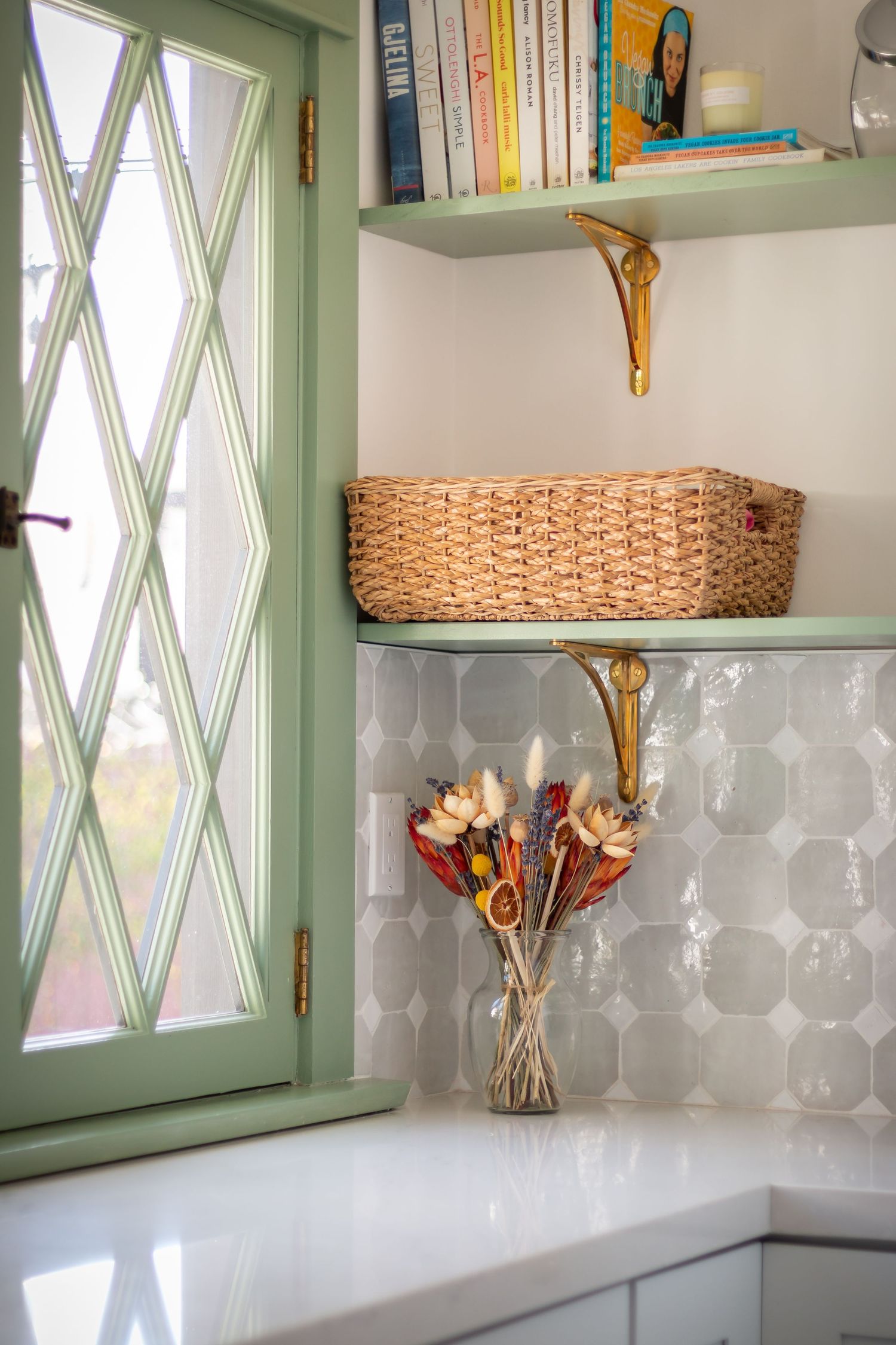 Kitchen shelf styling with woven basket, books, and dried flowers against diamond pane window.
