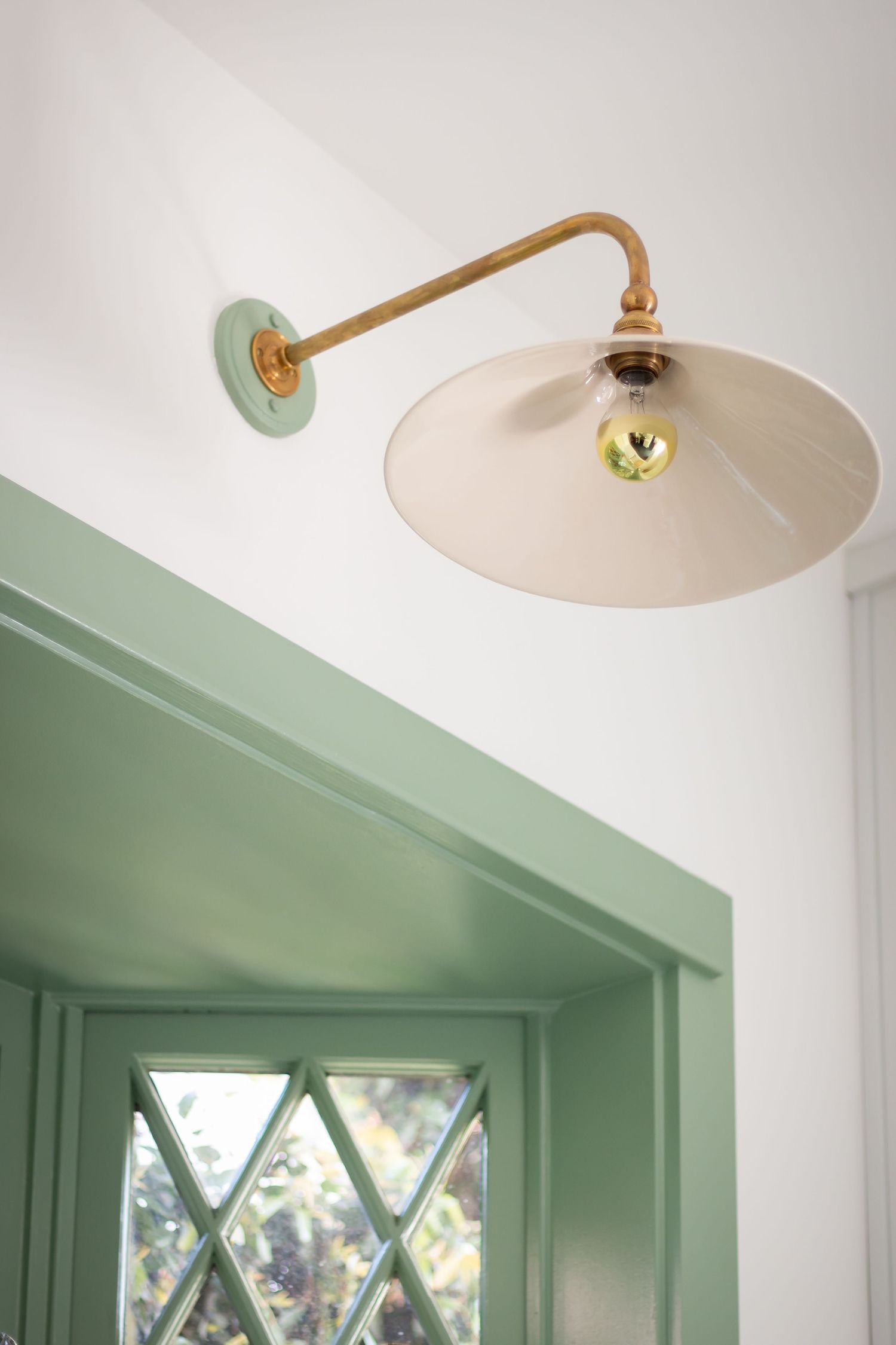Brass sconce light fixture with cream shade mounted above mint green trim.