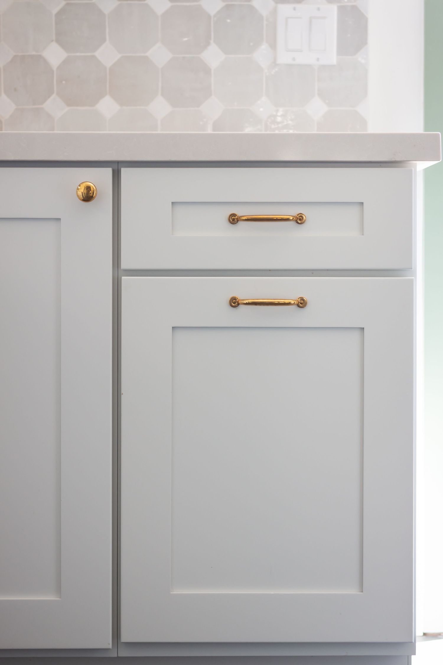 Detail shot of white shaker cabinet doors with brass pull handles and geometric tile backsplash.