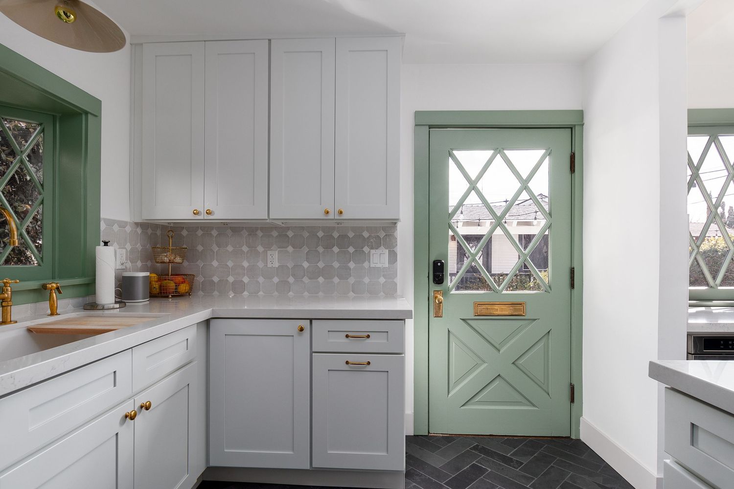 Bright kitchen with mint green Dutch door and white cabinetry features brass hardware accents.