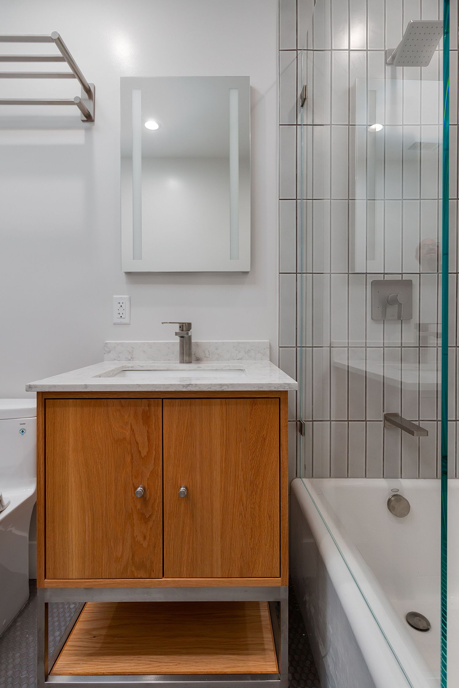 Minimalist bathroom design featuring wooden vanity, white tile walls, and glass shower partition.