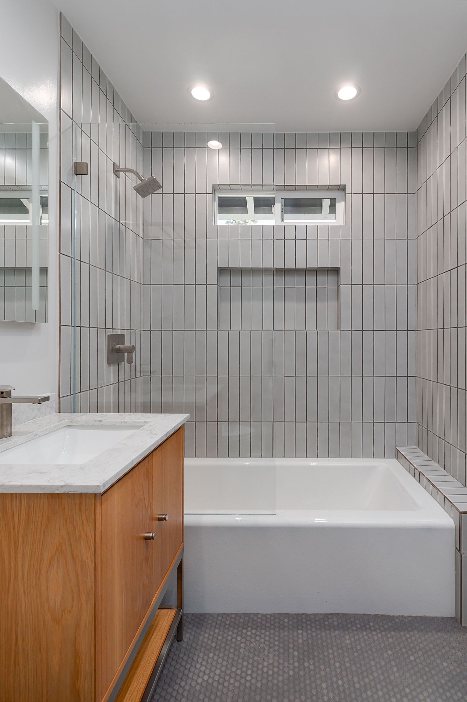 Modern bathroom with gray tile walls, wooden vanity, and white countertop showcases clean lines.