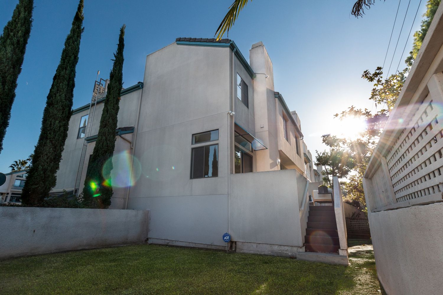 Exterior view of white modern house with tall cypress trees and landscaped yard.