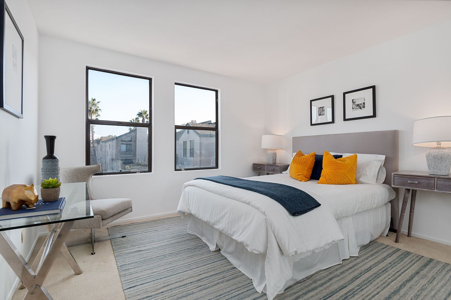 Contemporary white bedroom with large windows, gray accents, and orange throw pillows.