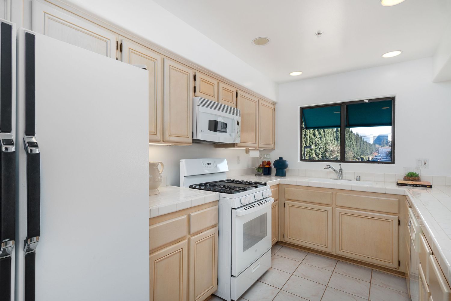Long galley kitchen with light wood cabinets, white appliances, and recessed lighting.