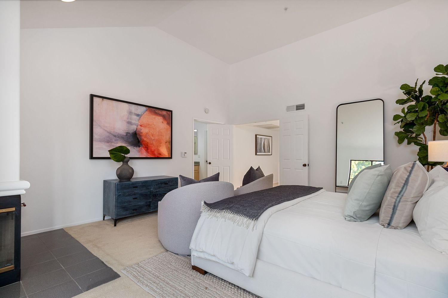 Modern bedroom with white walls, large windows, and minimalist decor featuring natural light and indoor plants.