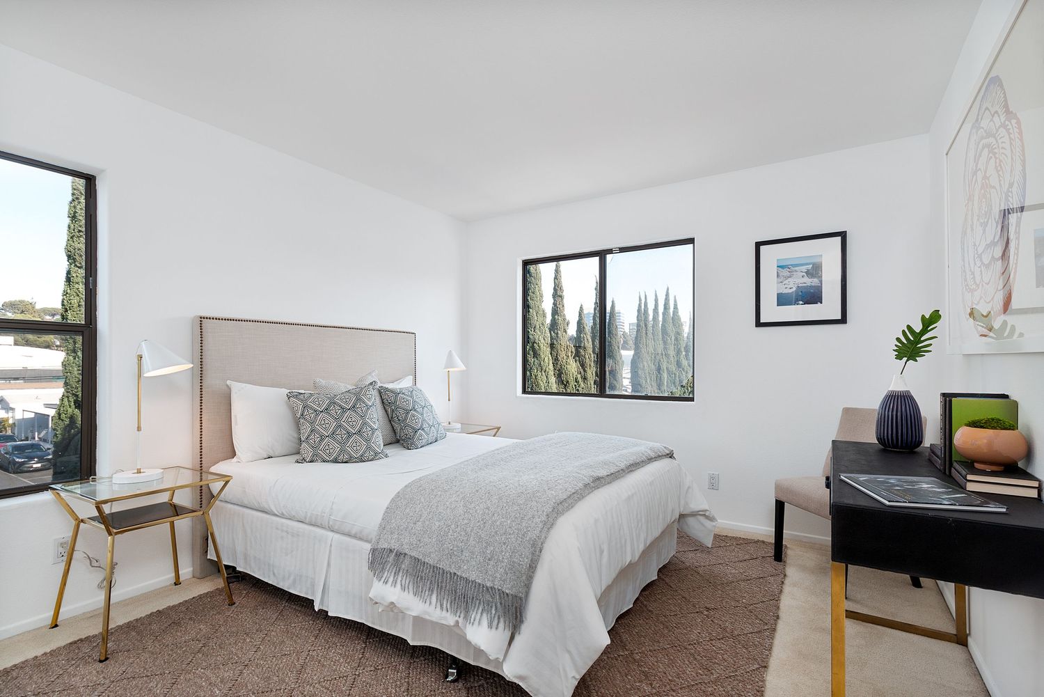 Spacious white bedroom with grey bedding, modern furnishings, and large windows providing natural light.