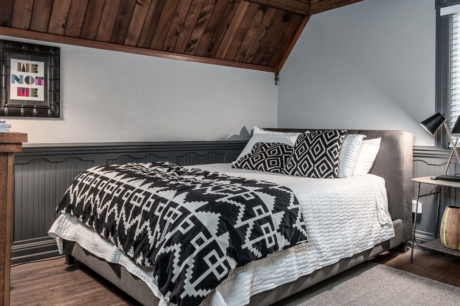 Bedroom with sloped wooden ceiling featuring black and white geometric bedding and modern decor.