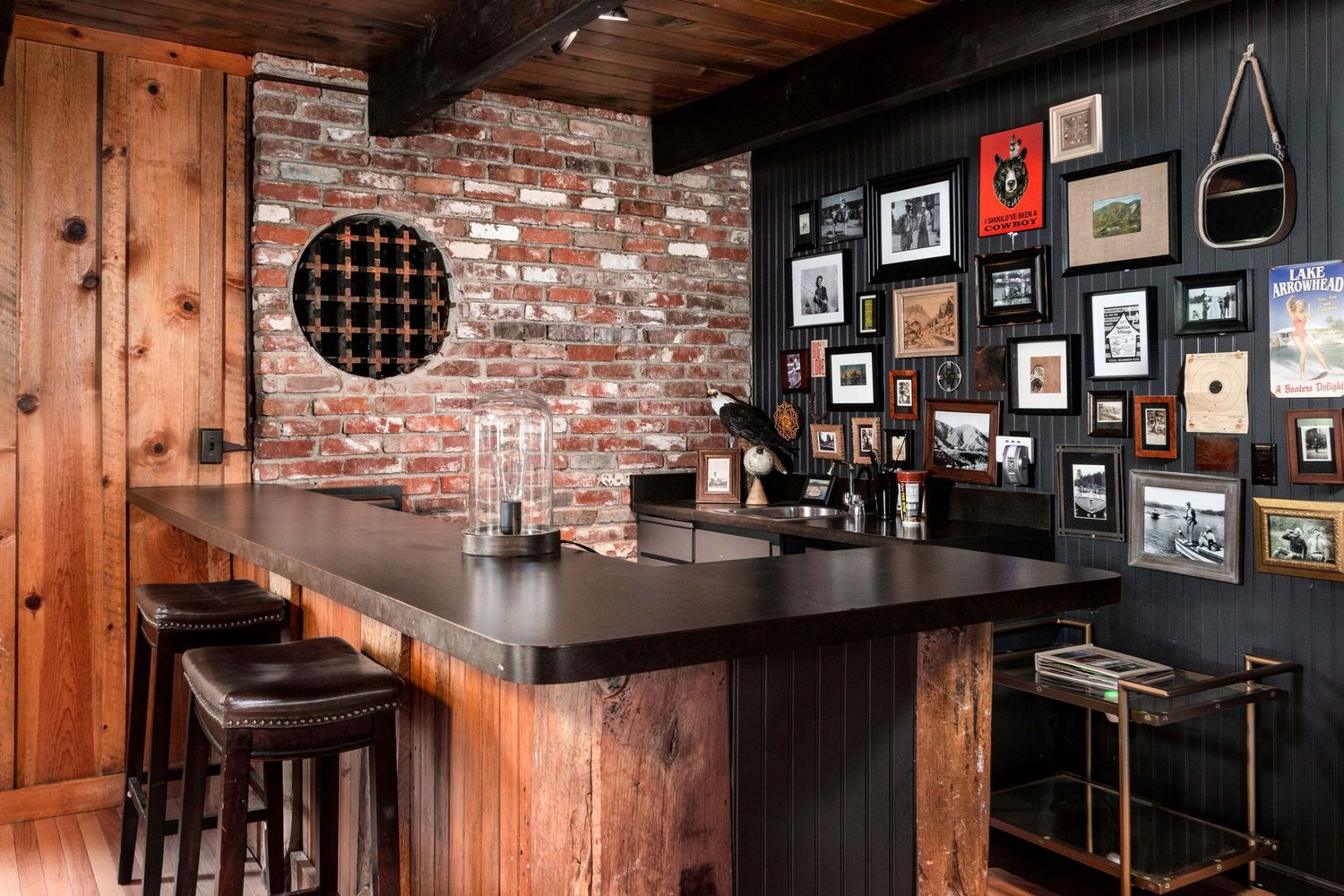 Rustic bar area with exposed brick wall, wooden paneling, and vintage decor displayed on walls.