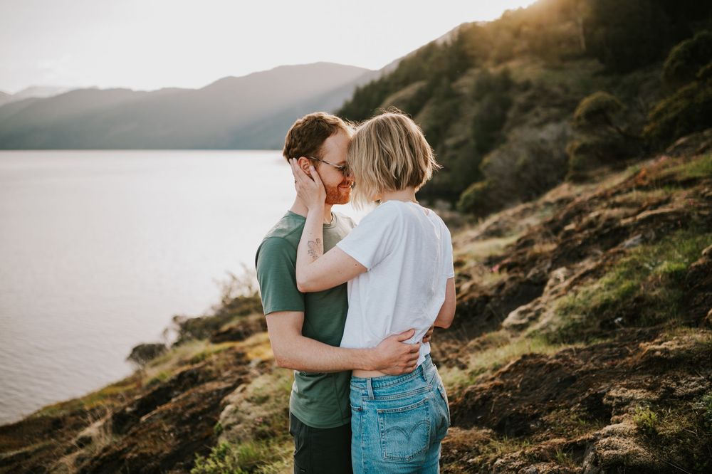 Couple hugging during their engagement session at Comox Lake Bluffs, warm light and mountain views behind them