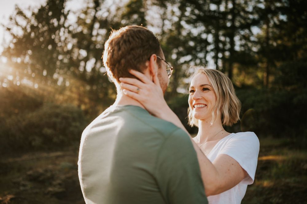 Close-up of couple embracing laughing with lake and mountains in background, candid golden hour engagement photo on Vancouver Island