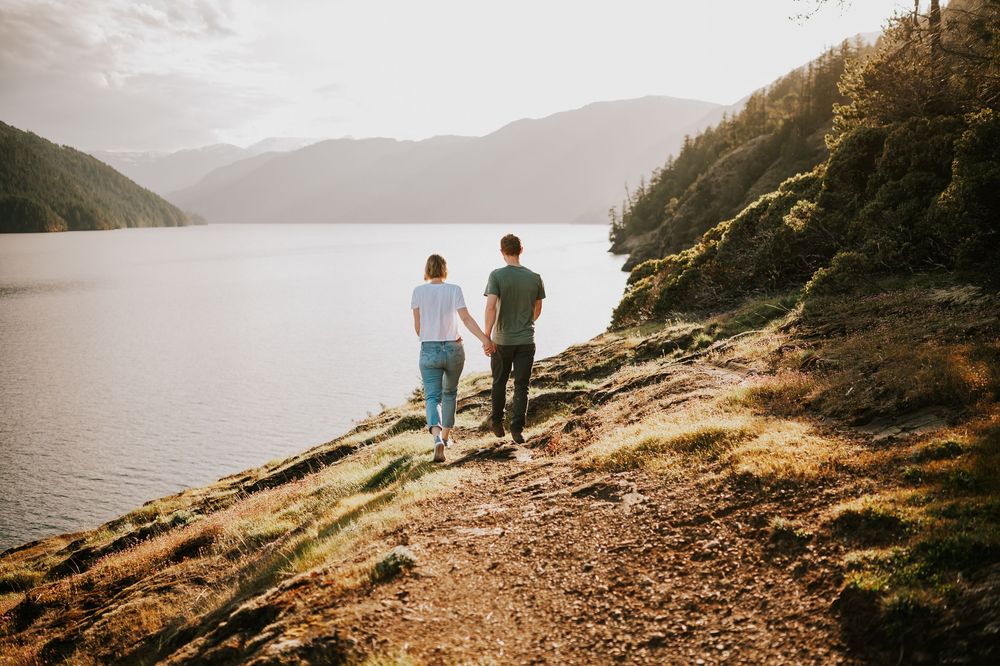 Couple walking hand in hand along Comox Lake Bluffs during golden hour with lake and mountain views in the background