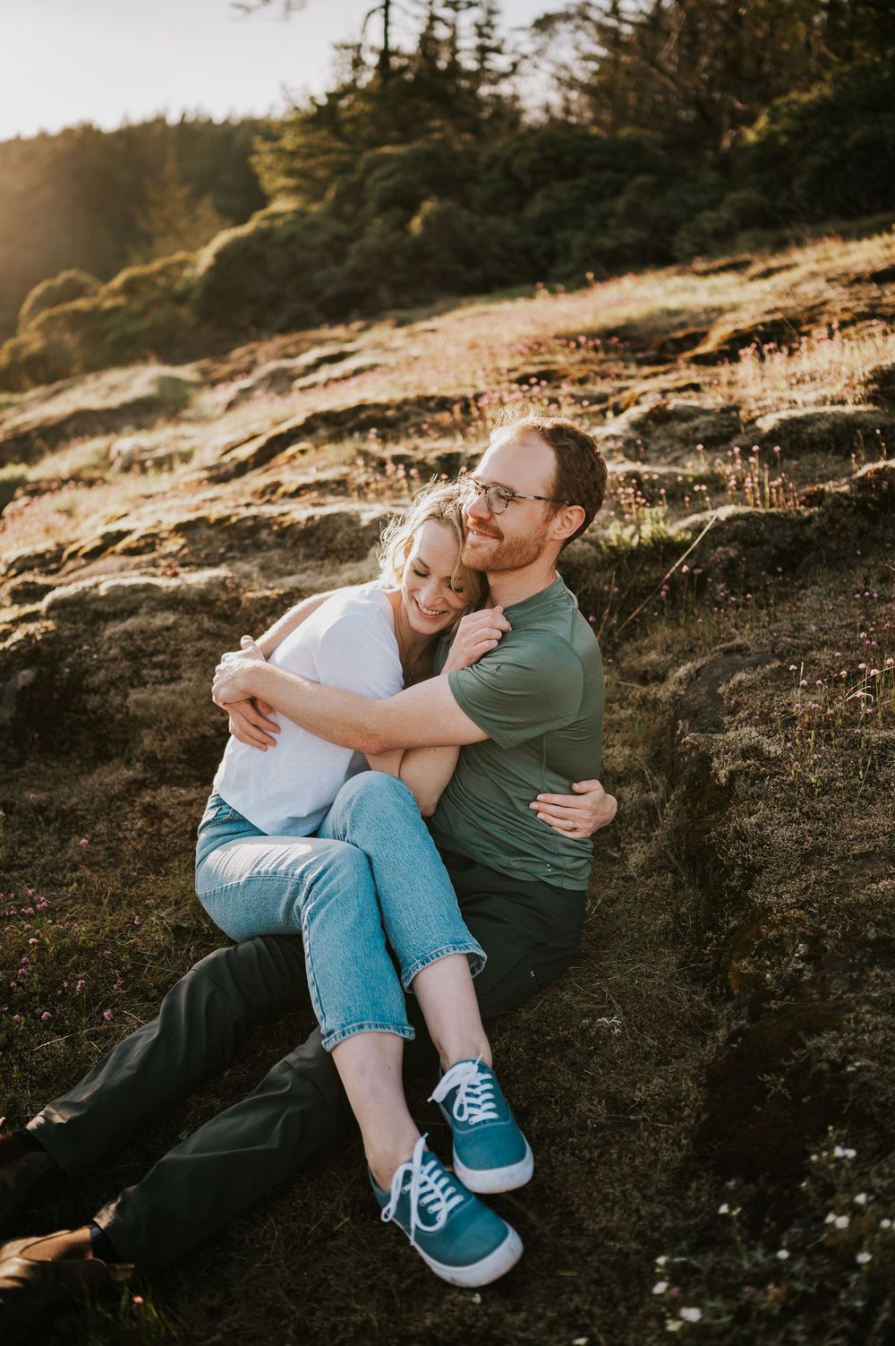 Couple sitting close together on rocky ledge at Comox Lake, relaxed moment during adventure session in each others arms