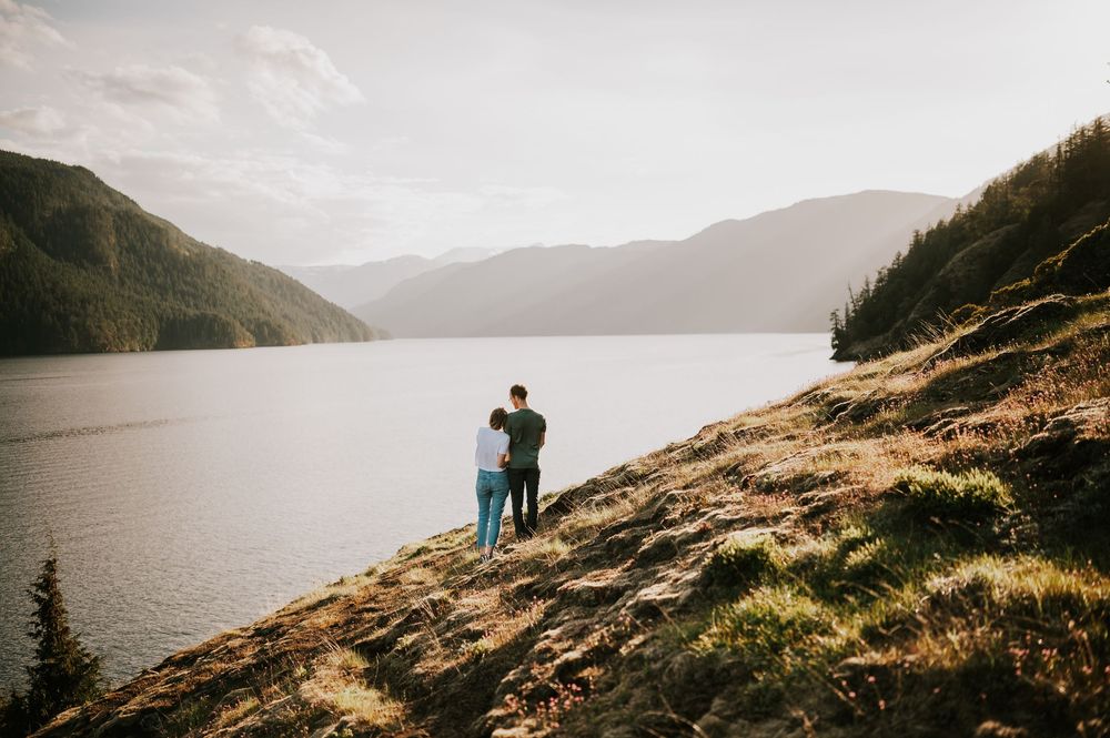 Couple embracing each other on Comox Lake Bluffs during golden hour with lake and mountain views in the background