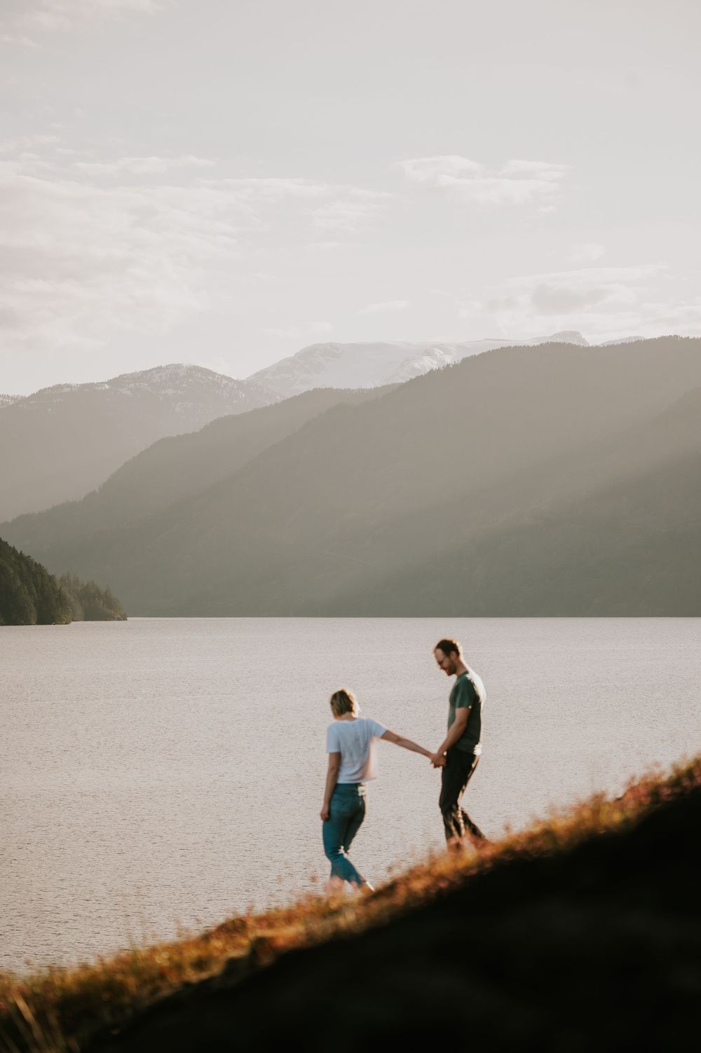 Couple walking hand in hand along Comox Lake Bluffs during golden hour with lake and mountain views in the background