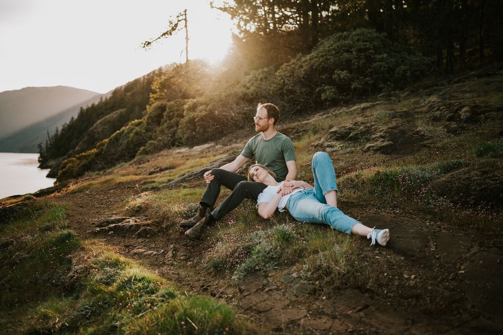 Soulful photography of couple sitting close together on rocky ledge at Comox Lake bluff location relaxed moment during engagement photoshoot