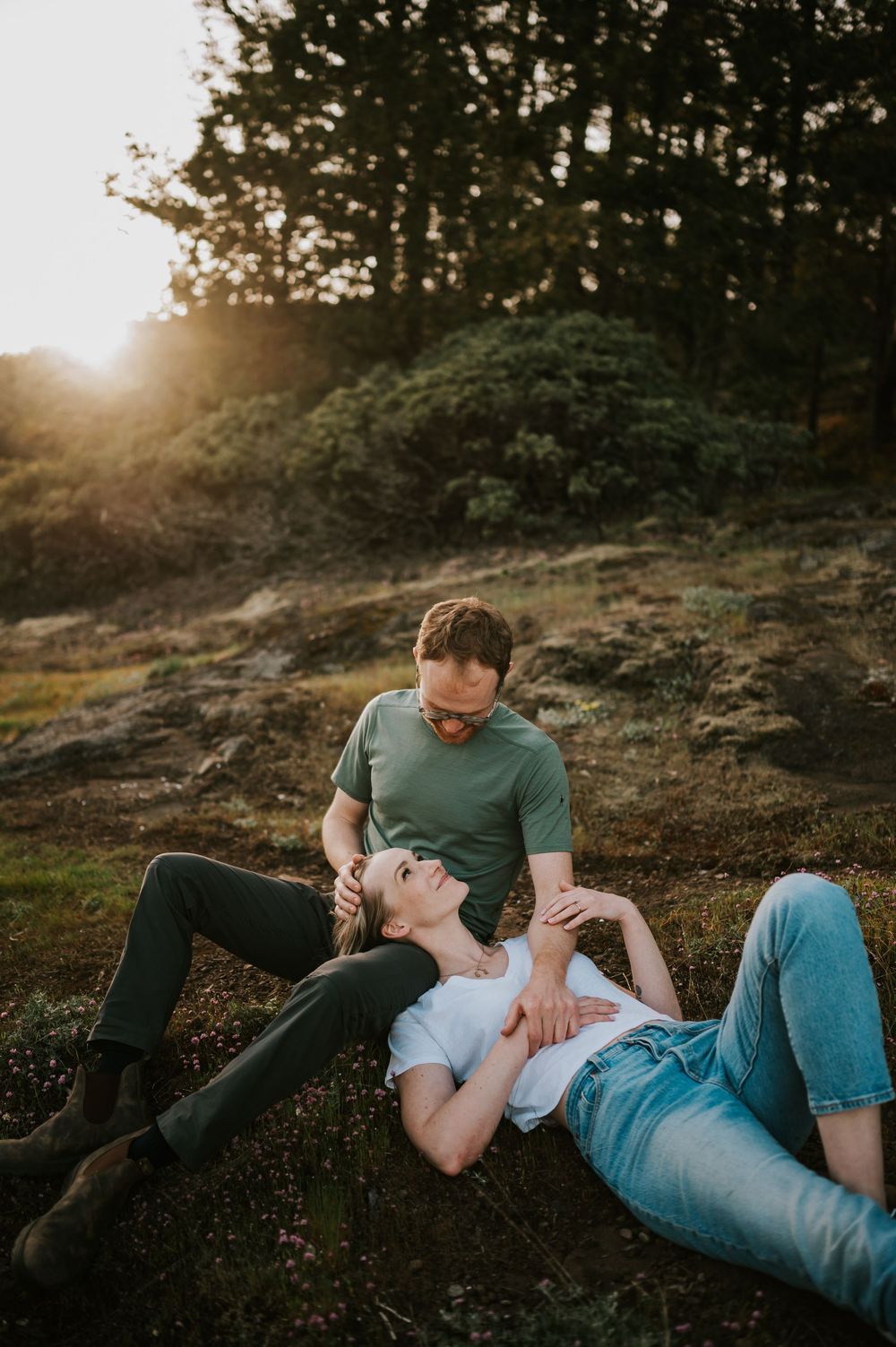 Couple sitting close together on rocky ledge at Comox Lake bluff location, relaxed moment during engagement photoshoot