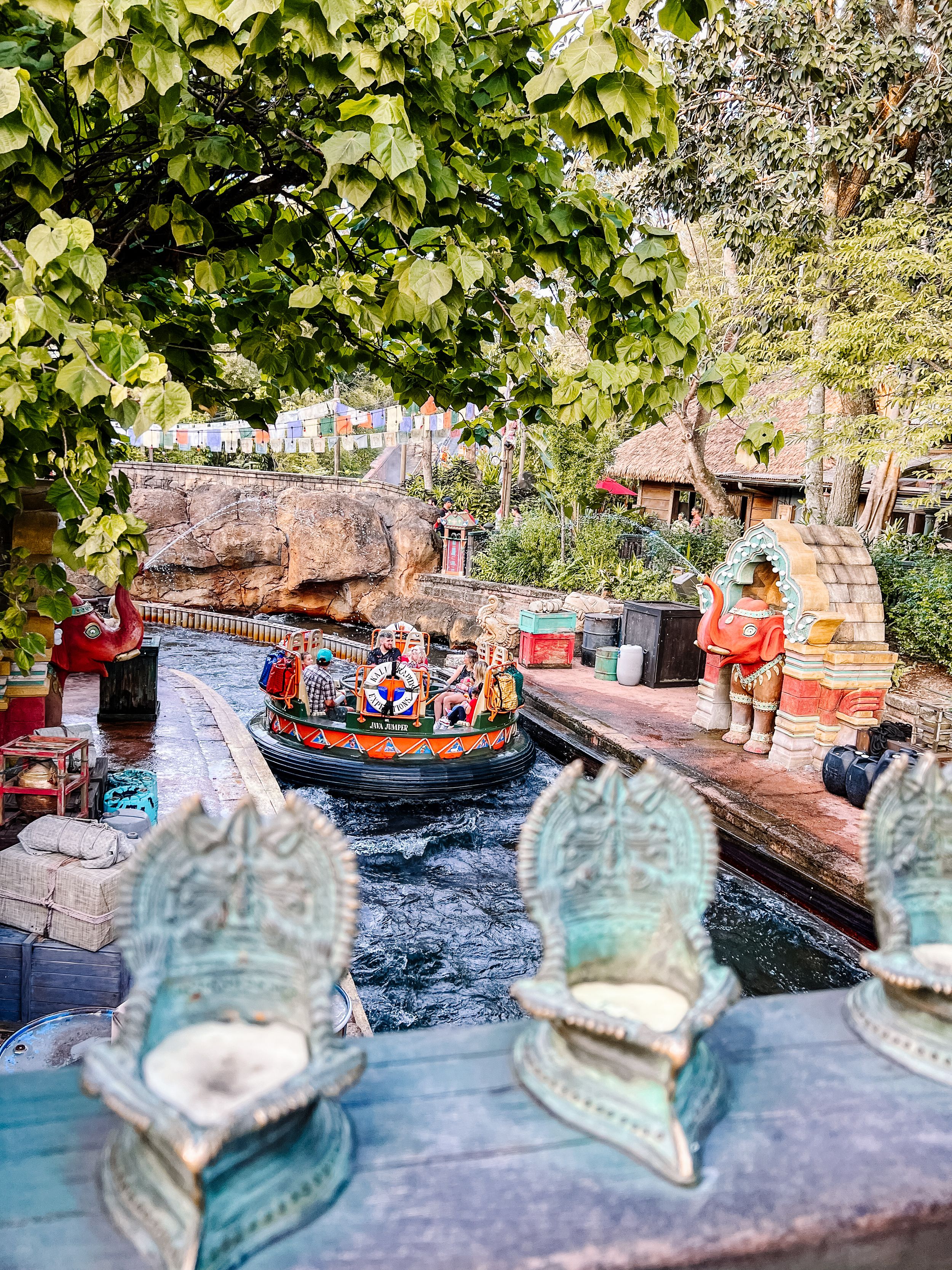 Riders enjoy a splashing adventure on a river raft ride through themed rockwork and decorative ornaments at a theme park.