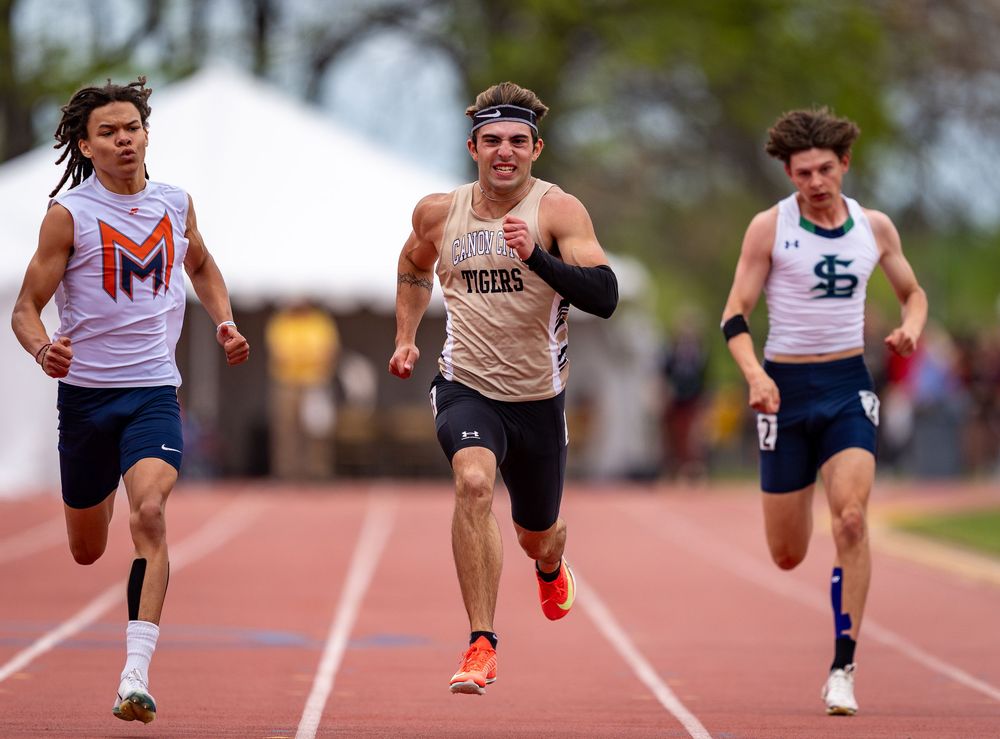 Three sprinters compete neck and neck in close race on outdoor track.