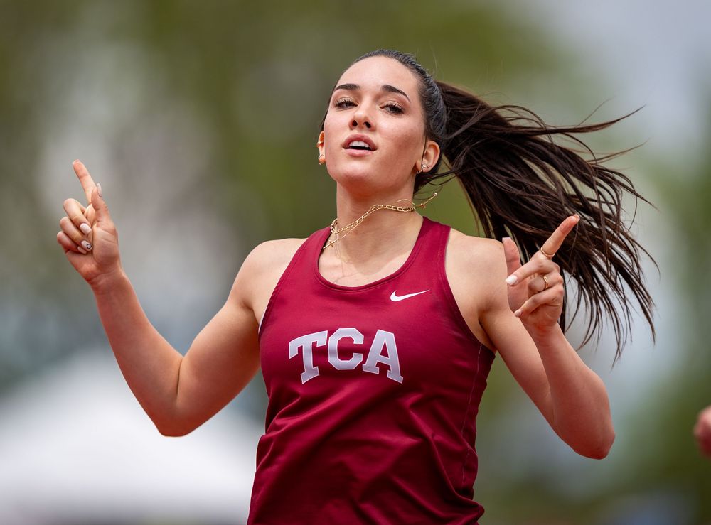 Track athlete in maroon TCA uniform celebrates during competition with hair flowing.