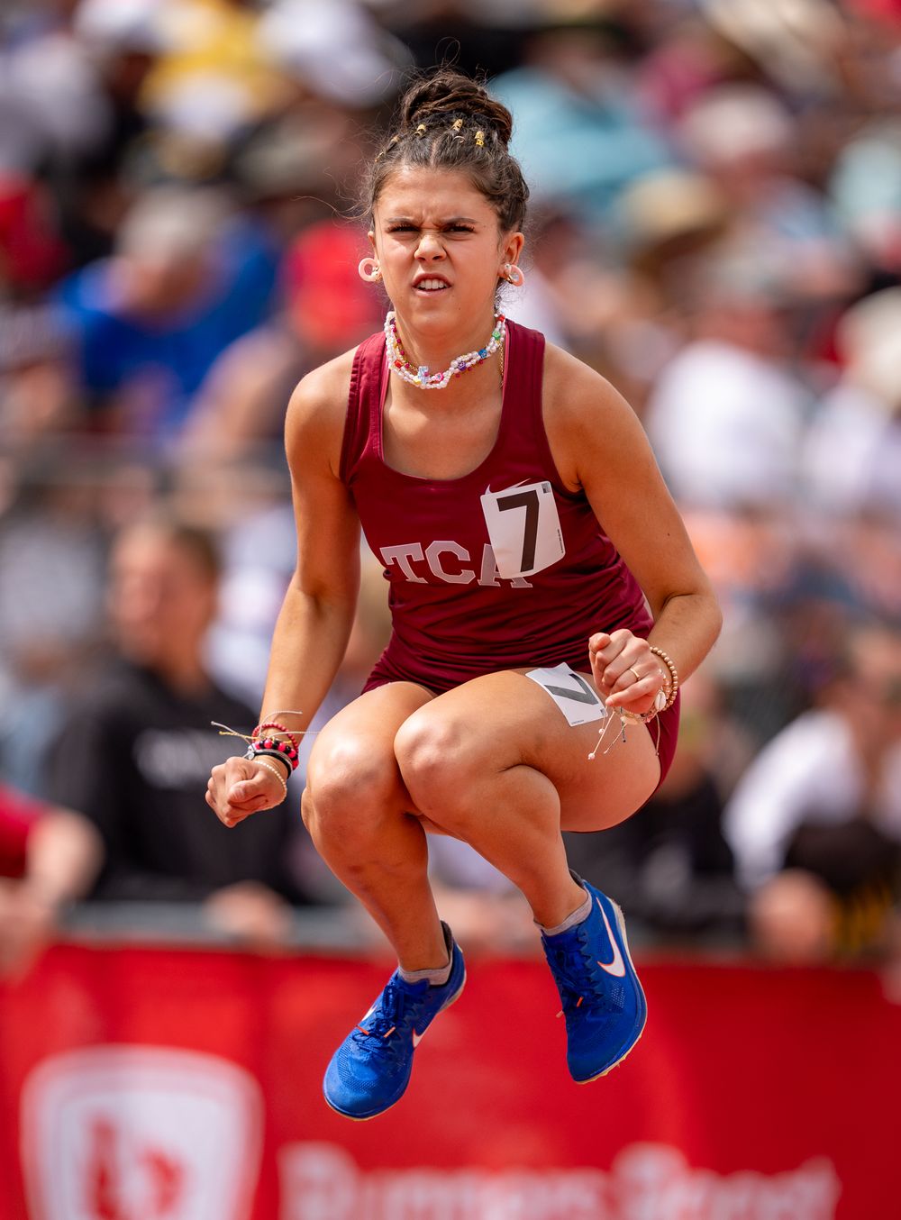 Track athlete in maroon uniform jumps during competition wearing blue sneakers.