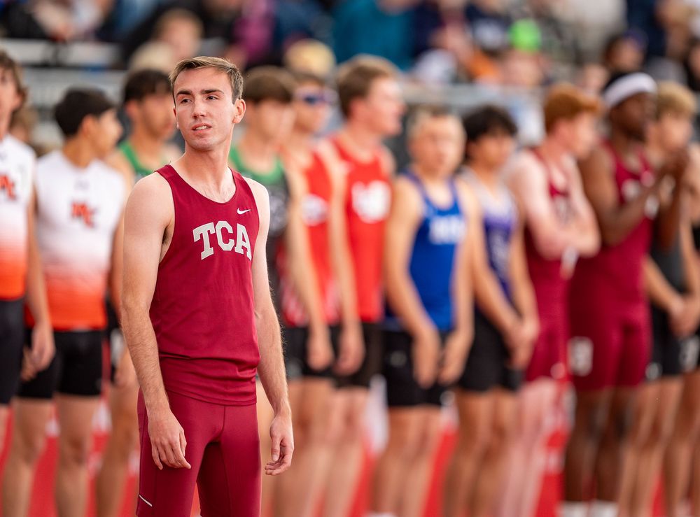 Athletes lined up at track meet wearing different colored uniforms.