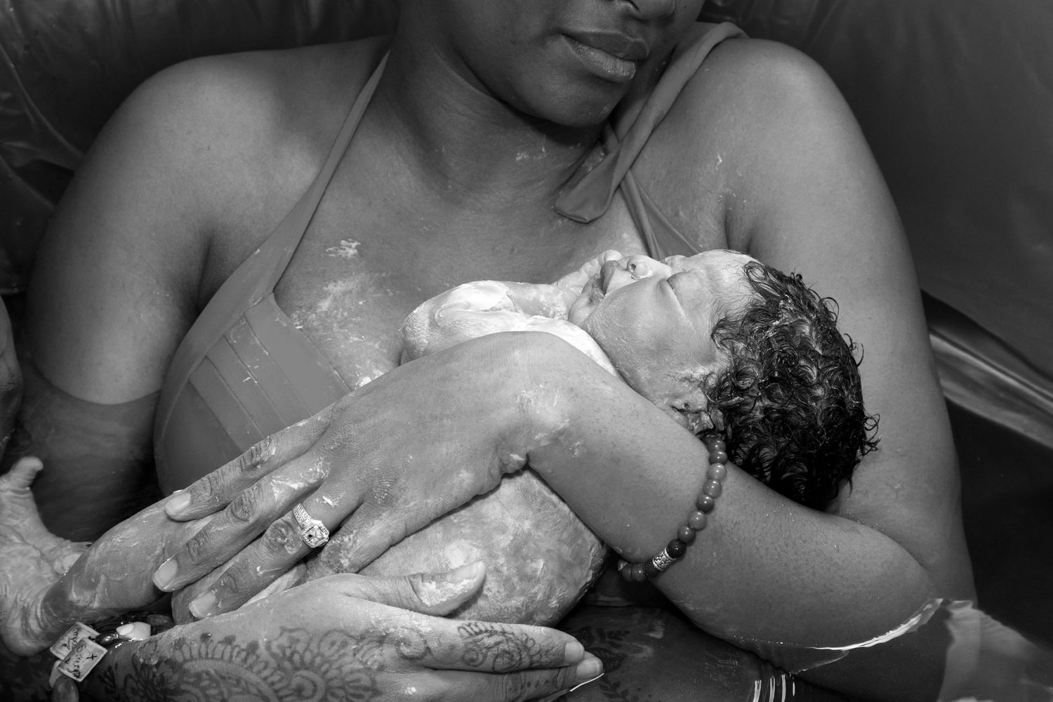 San Diego homebirth. San Diego Doula. A caregiver holds and comforts a small newborn baby in an intimate black and white portrait.