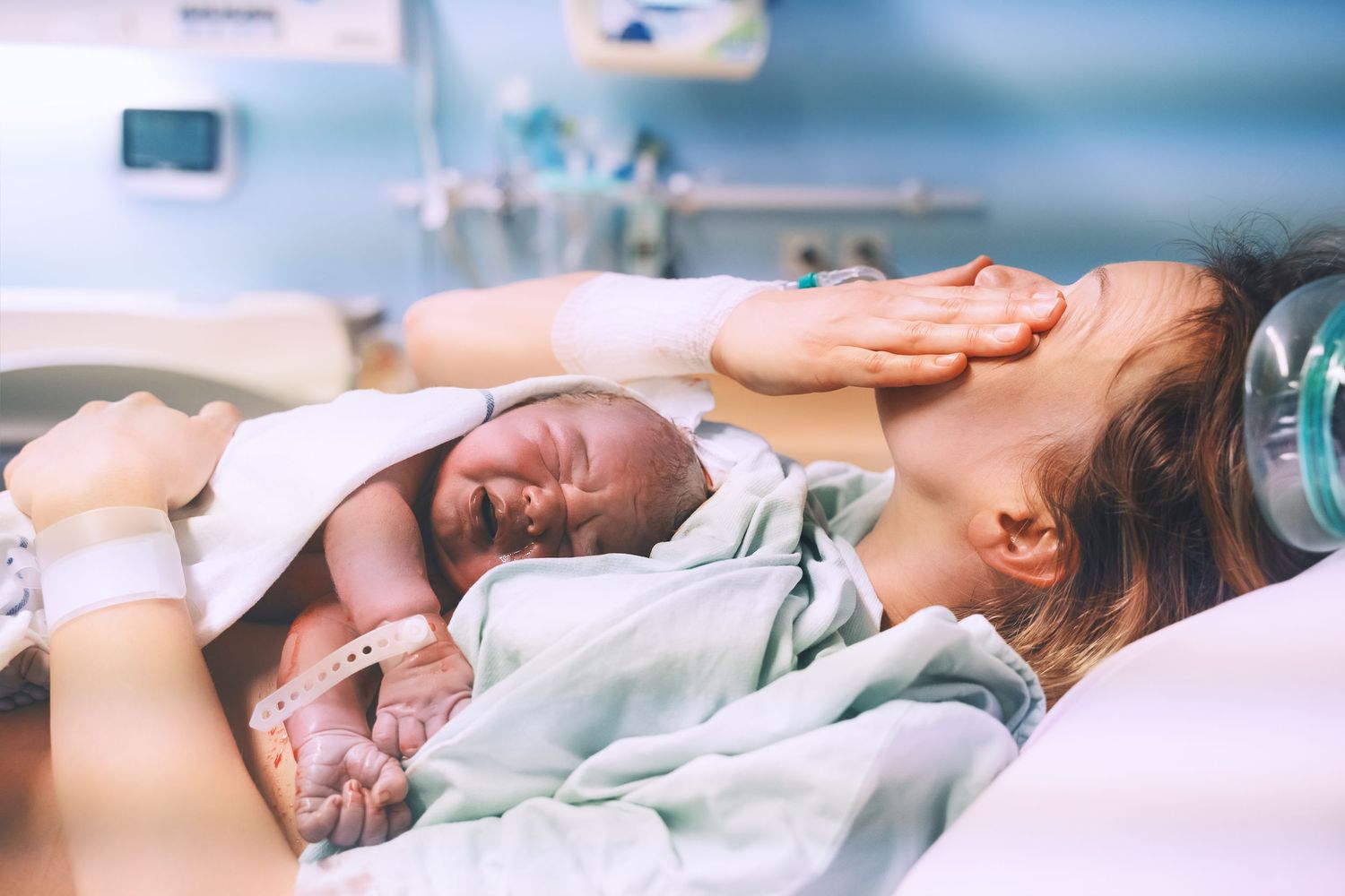 UCSD labor and delivery. Midwife, Doula. A tired mother rests with a newborn baby in a hospital bed after delivery.