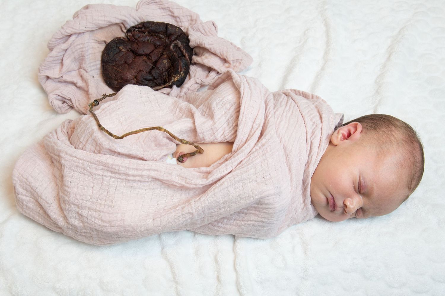 Homebirth San Diego, first 48. A sleeping newborn baby swaddled in a soft pink blanket lies peacefully on white fabric.