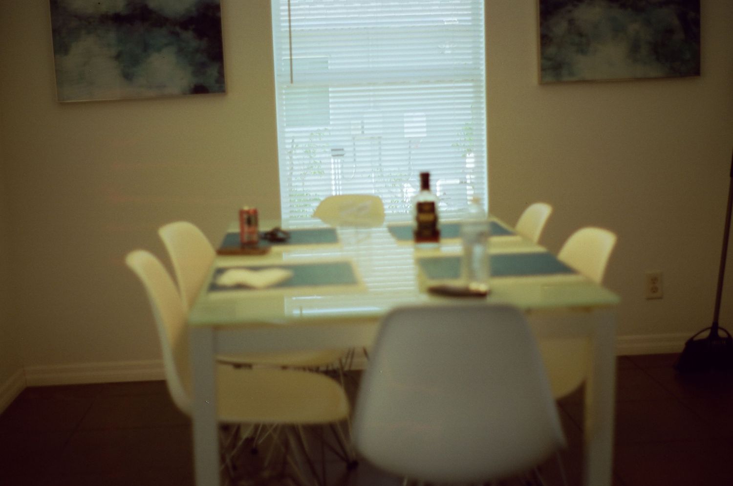 Retro-style dining room with white modern chairs around oval table, artwork on walls, and soft mood lighting.
