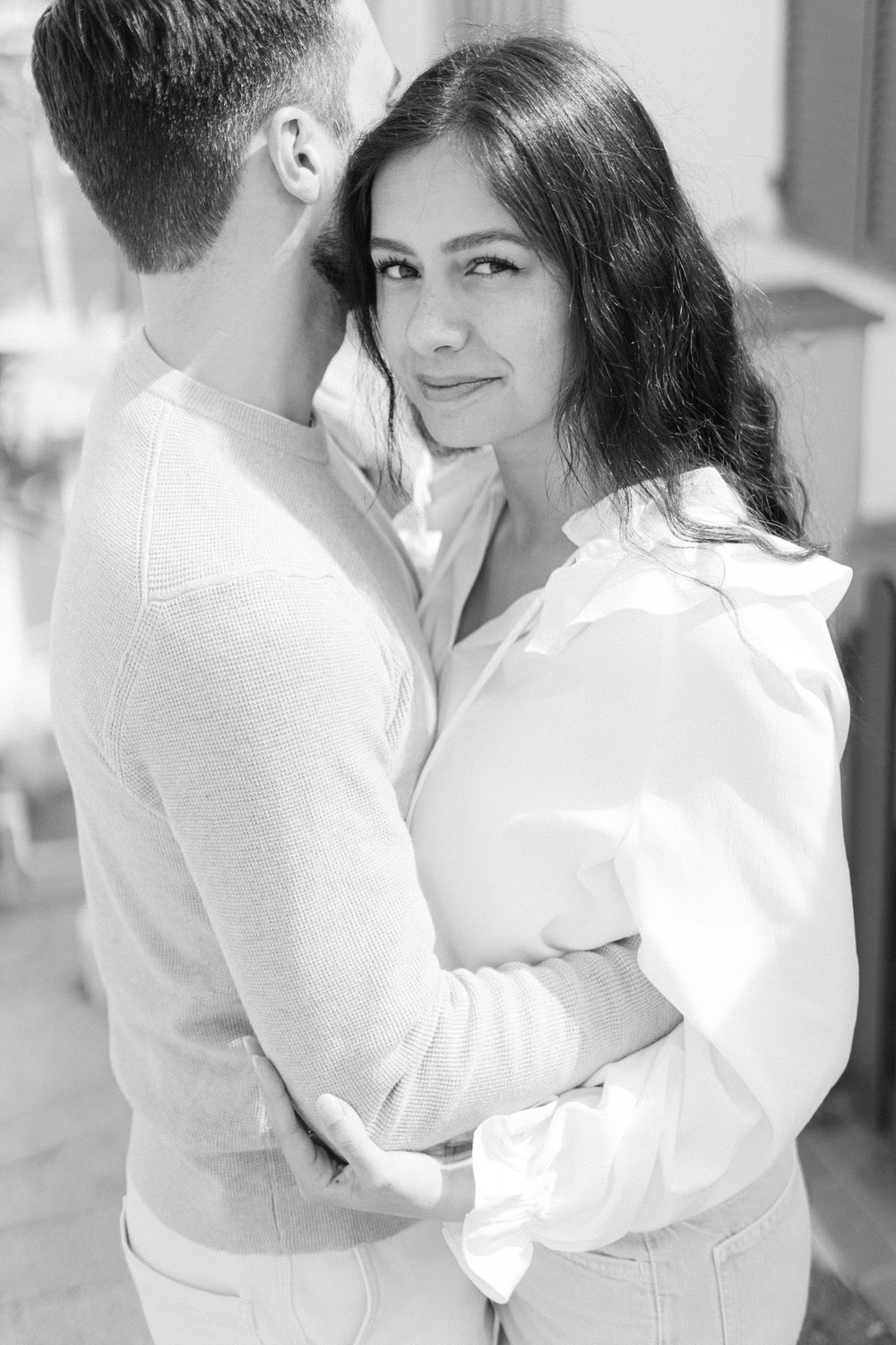 A romantic black and white portrait of a couple in white outfits embracing tenderly.