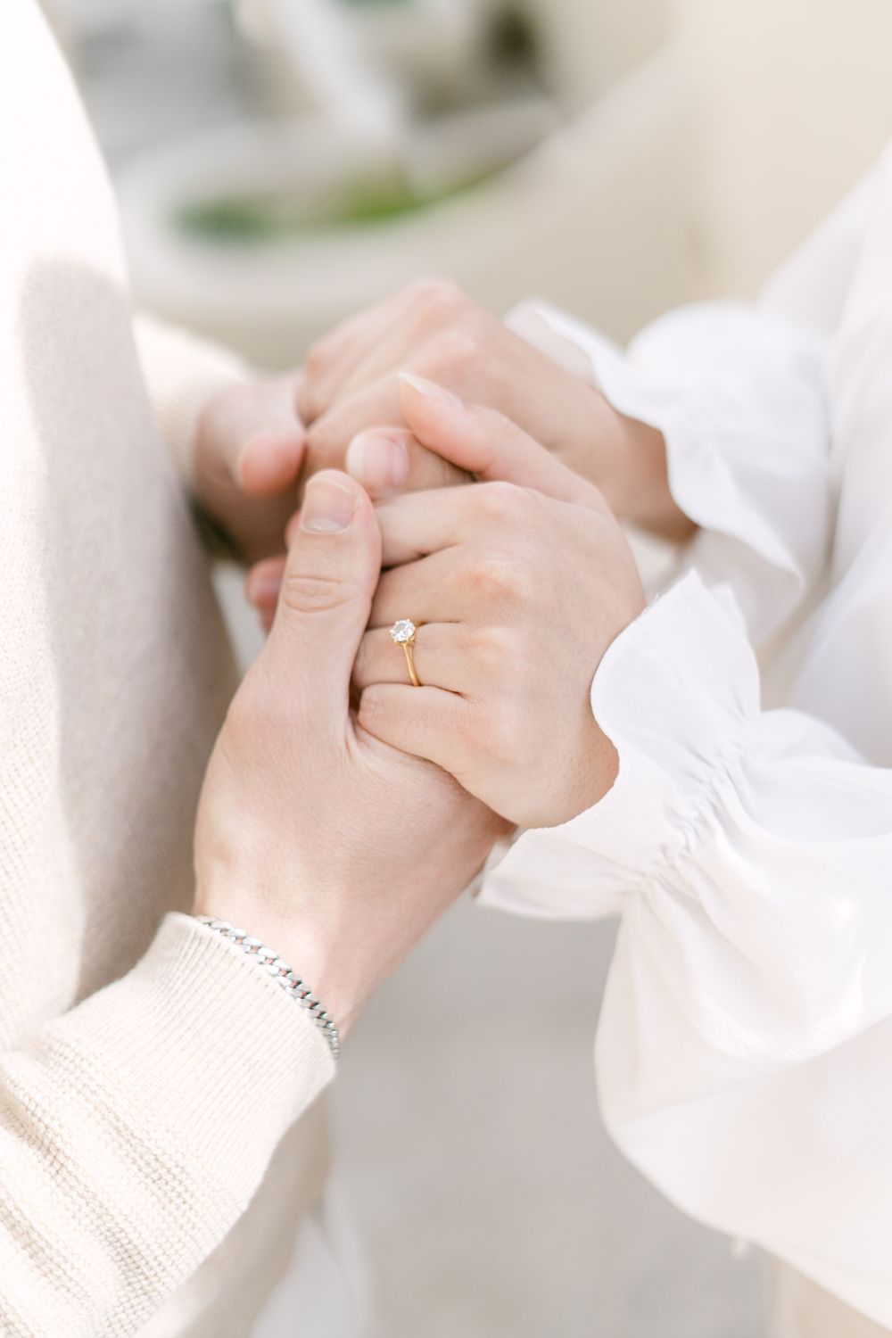 Close up of hands with engagement rings and white sleeves holding each other tenderly.
